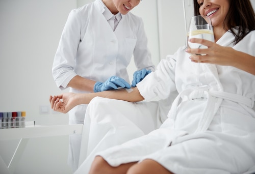 Female patient receiving IV therapy smiling while enjoying a refreshing and hydrating beverage. The professional and skilled staff at KP Aesthetics is delivering the IV to the patient.