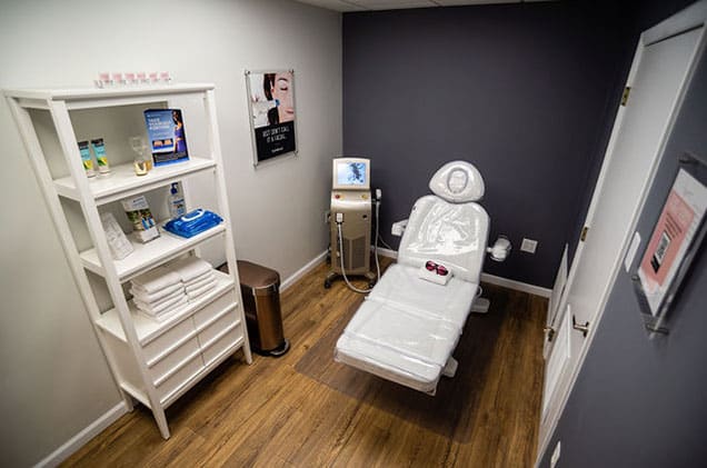 Bright and clean patient room at KP Aesthetics with white chair and wood floors.