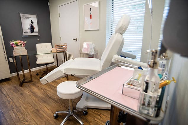 Bright and clean patient room at KP Aesthetics with white chair and wood floors.