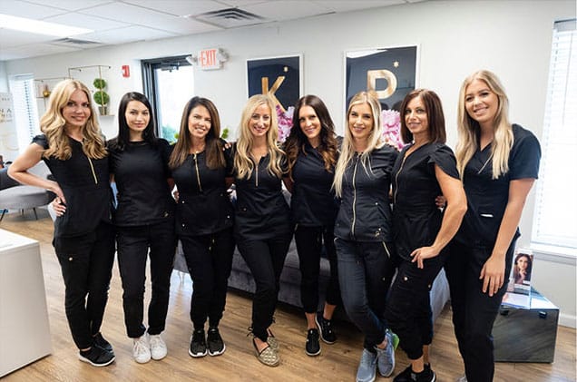 Staff of KP Aesthetics pose together in their professional uniforms all smiling and looking inviting.