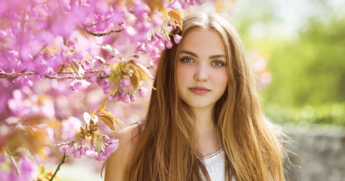 A stunning woman's face with blonde hair standing close to a treeflower.