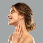 A stunning woman clutching her flawless neck in a side view